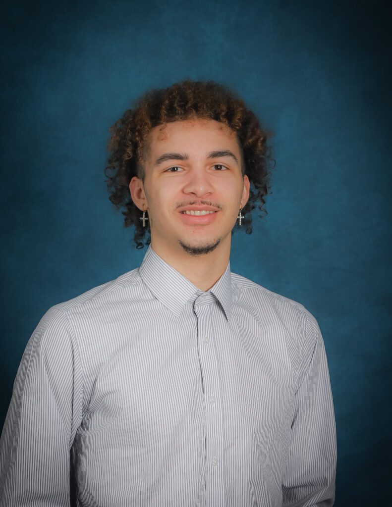 Kinesiologist, Noah Pemberton HKin headshot wearing a striped button up shirt in front of blue wall